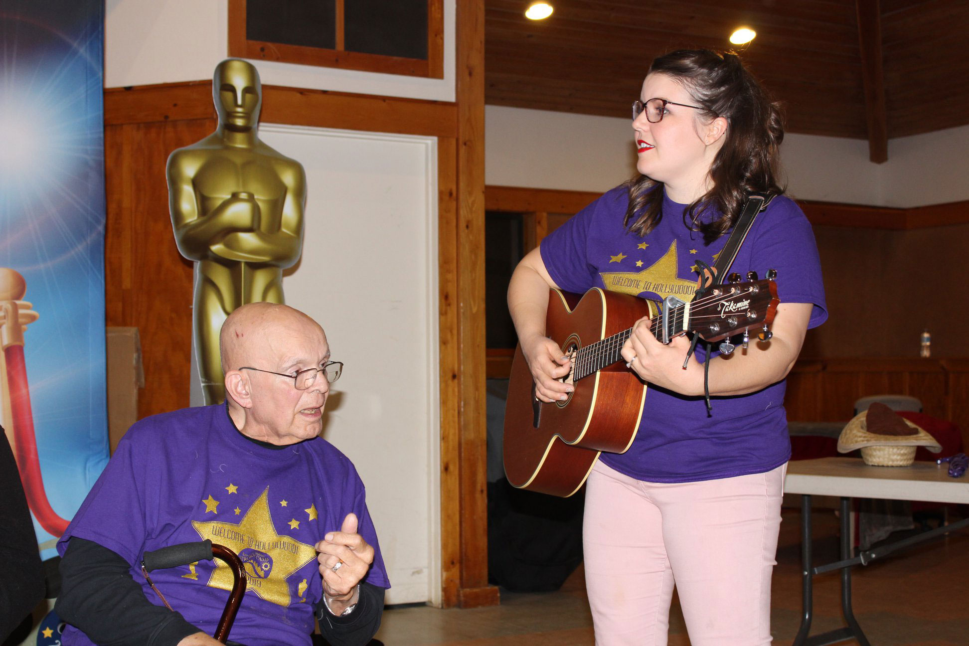 Young woman playing guitar to a senior man in a wheelchair
