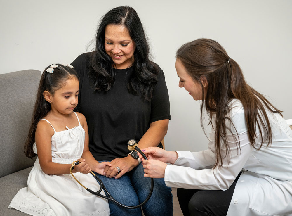 Female pediatrician treating young girl, who is with her mom