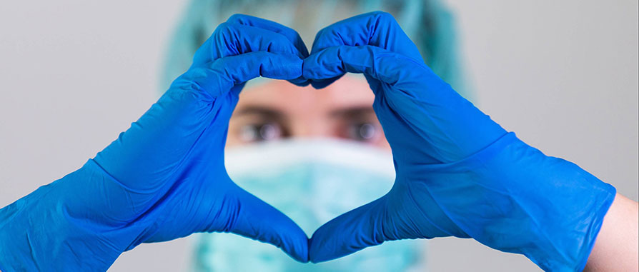 surgeon with blue gloves making heart symbol with hands