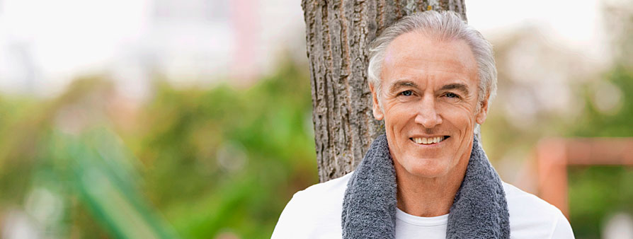 senior man standing in front of a tree with a towel around his neck