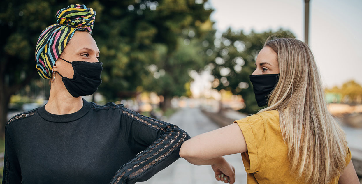 Two women wearing masks elbow bumping